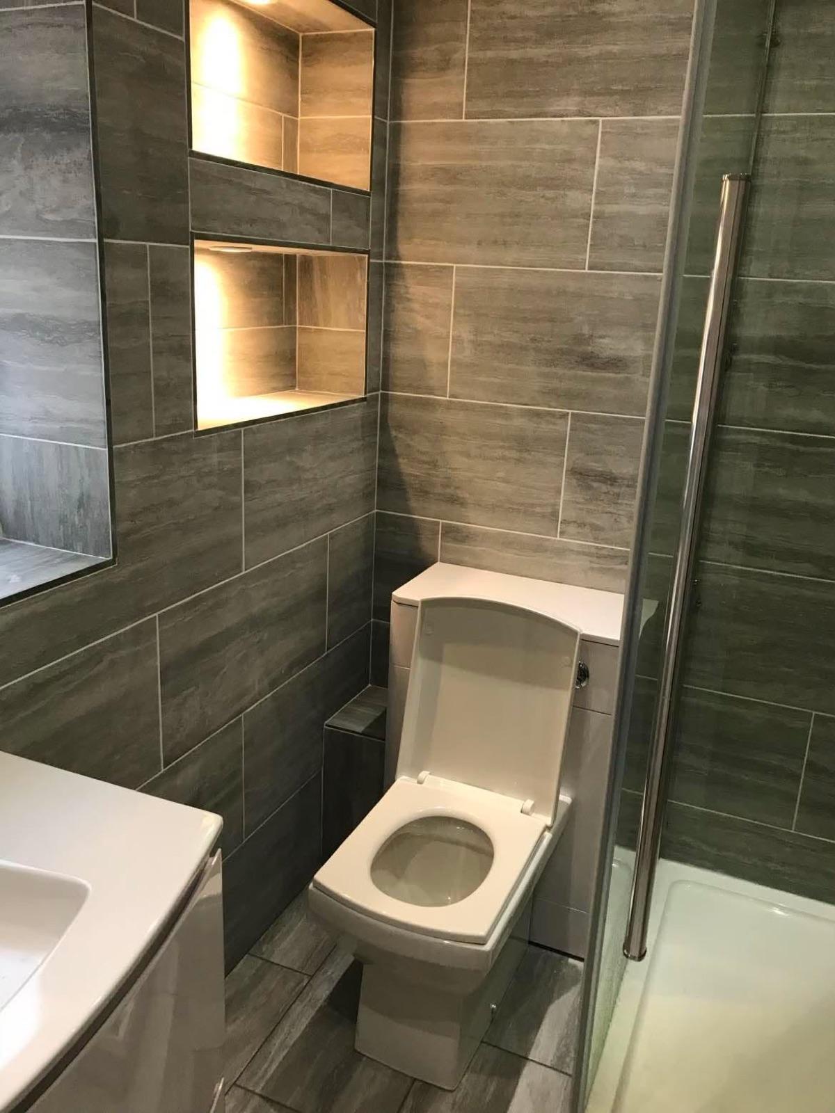 Finished shower room in Nuneaton by Chris Builder — dark wood-effect tiling with a lit display niche above the WC.
