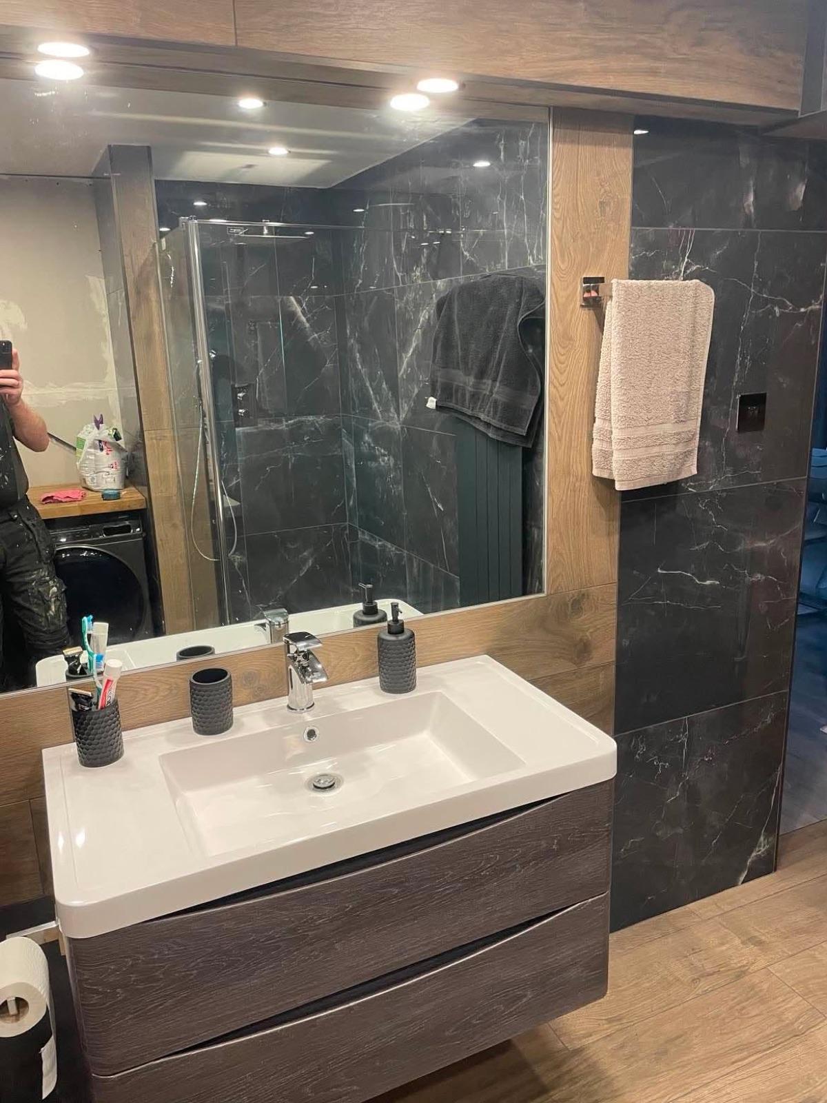 Finished bathroom vanity — dark marble-effect wall, wood-grain unit and white basin.