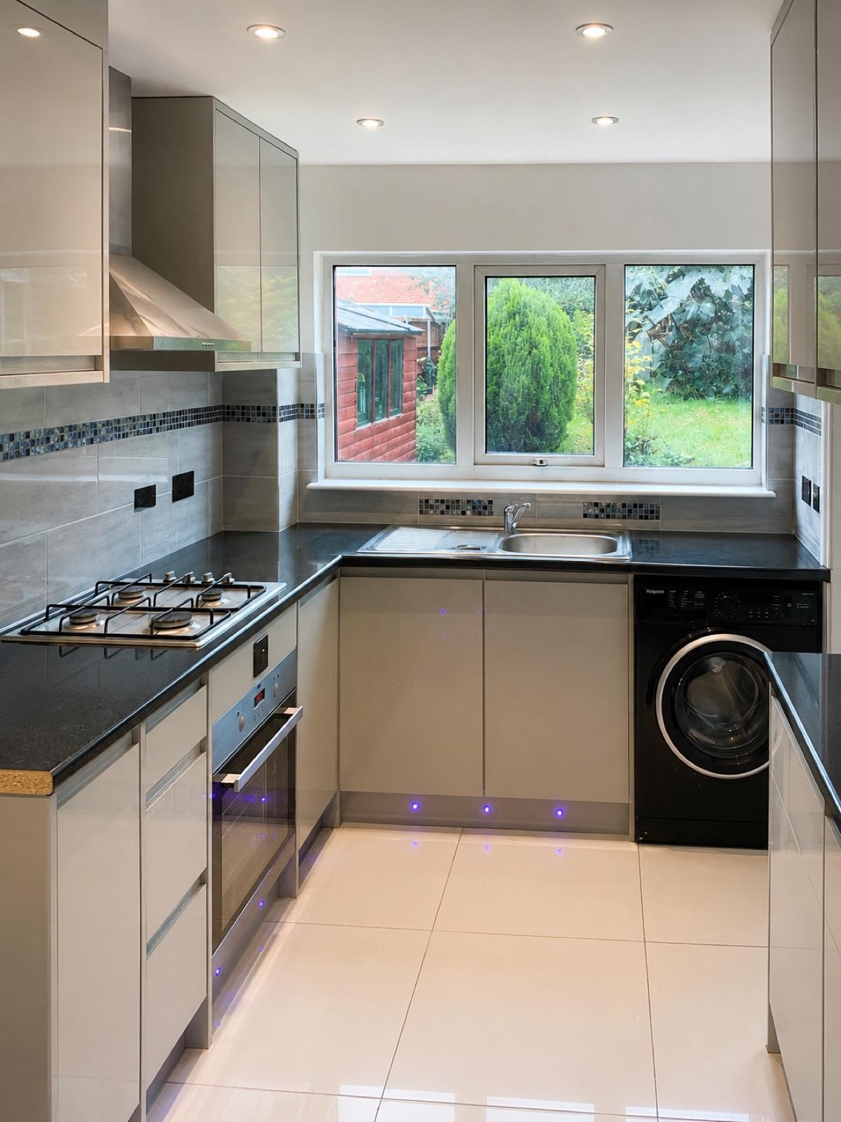 A re-planned kitchen finished in grey units with a black worktop and a garden window.