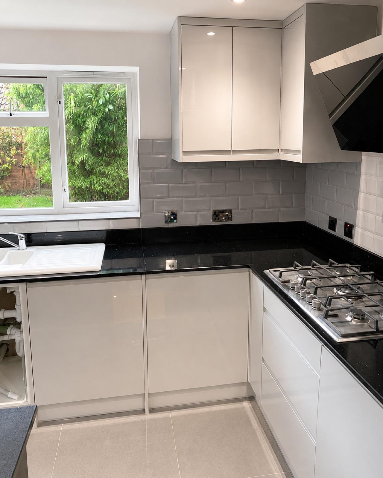 Finished sink and hob corner — white gloss units and black granite worktop.